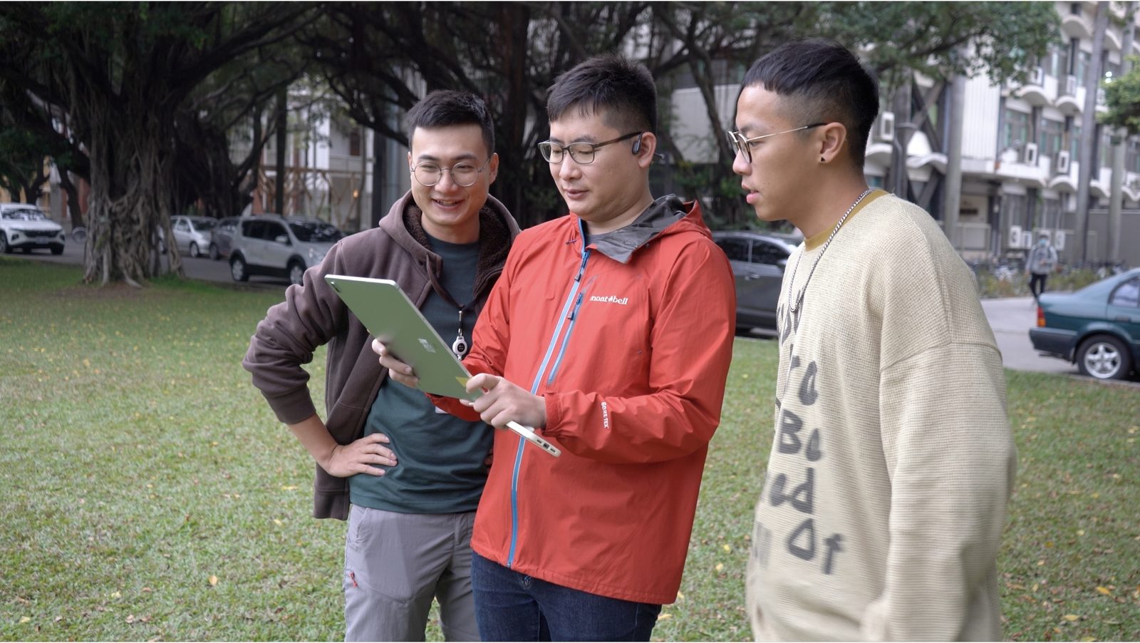 Three testers gathered around a tablet under the banyan canopy, looking at the AR maze together.