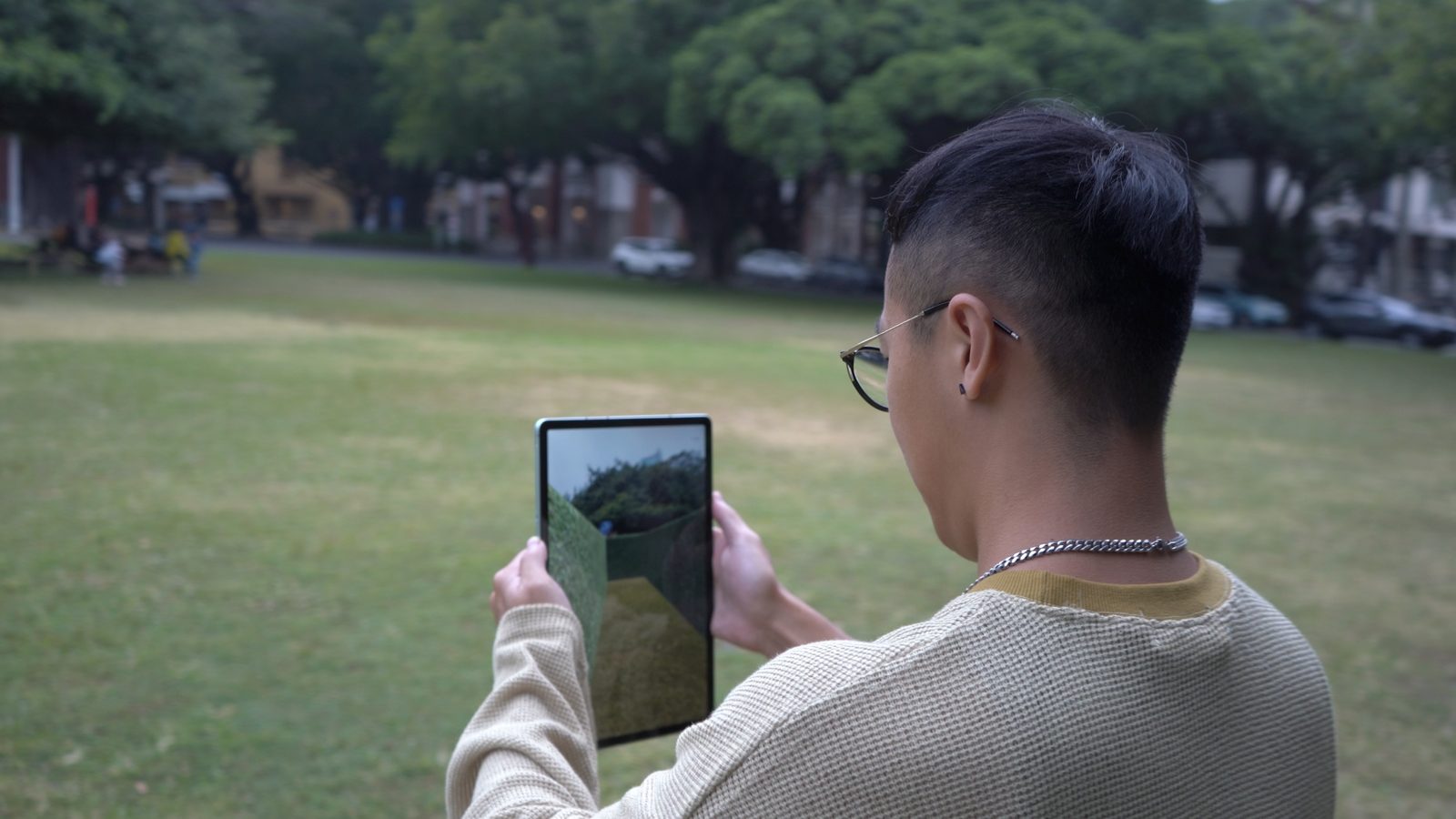 Tester in red jacket holding a phone, looking down at the screen on the grass.
