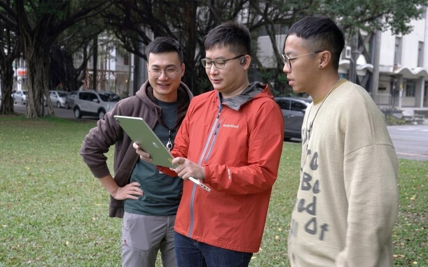 榕易迷路 AR Maze — testers in NCKU Banyan Garden hold a tablet showing the AR hedge maze overlaid on real grass.