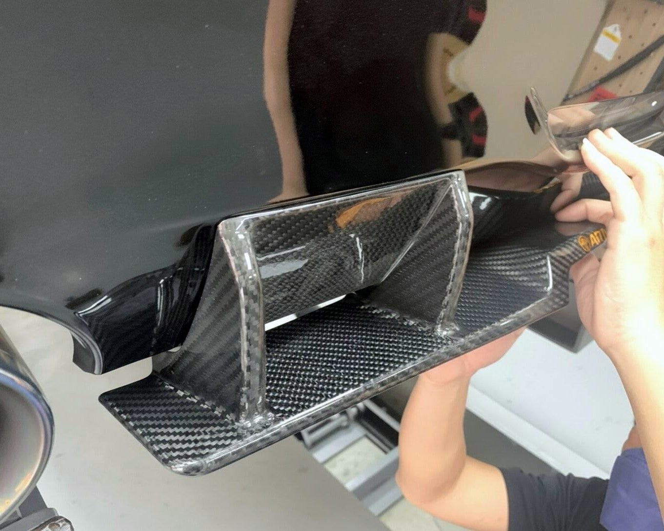 Hands fitting a carbon fiber piece against a black car body to check fit.