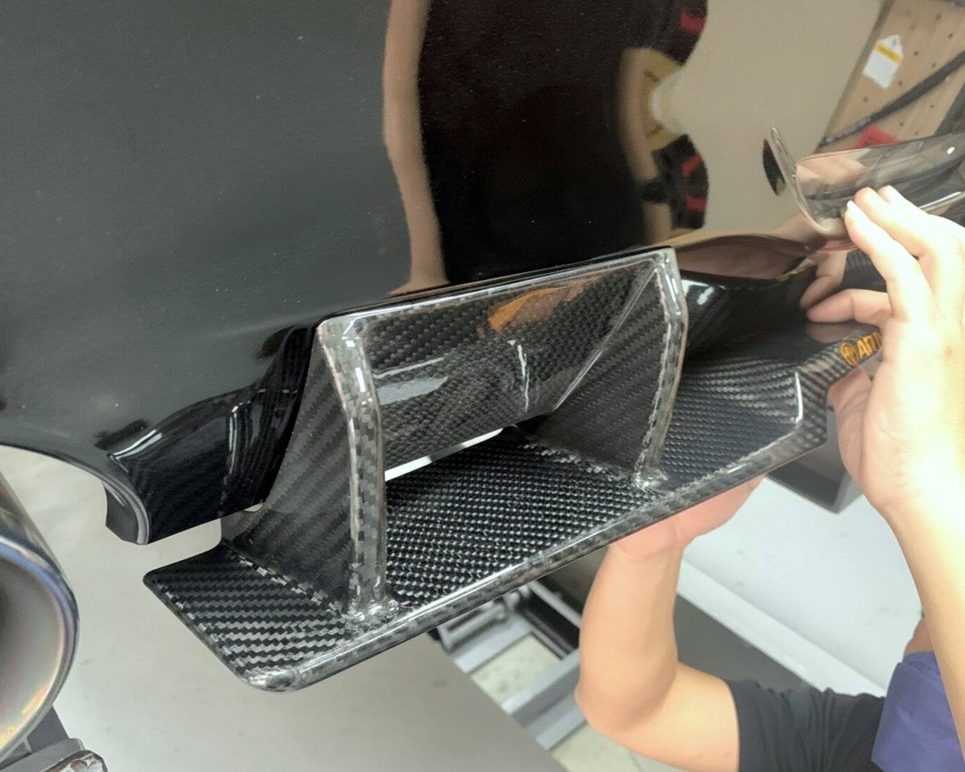 Hands fitting a carbon fiber piece against a black car body to check fit.
