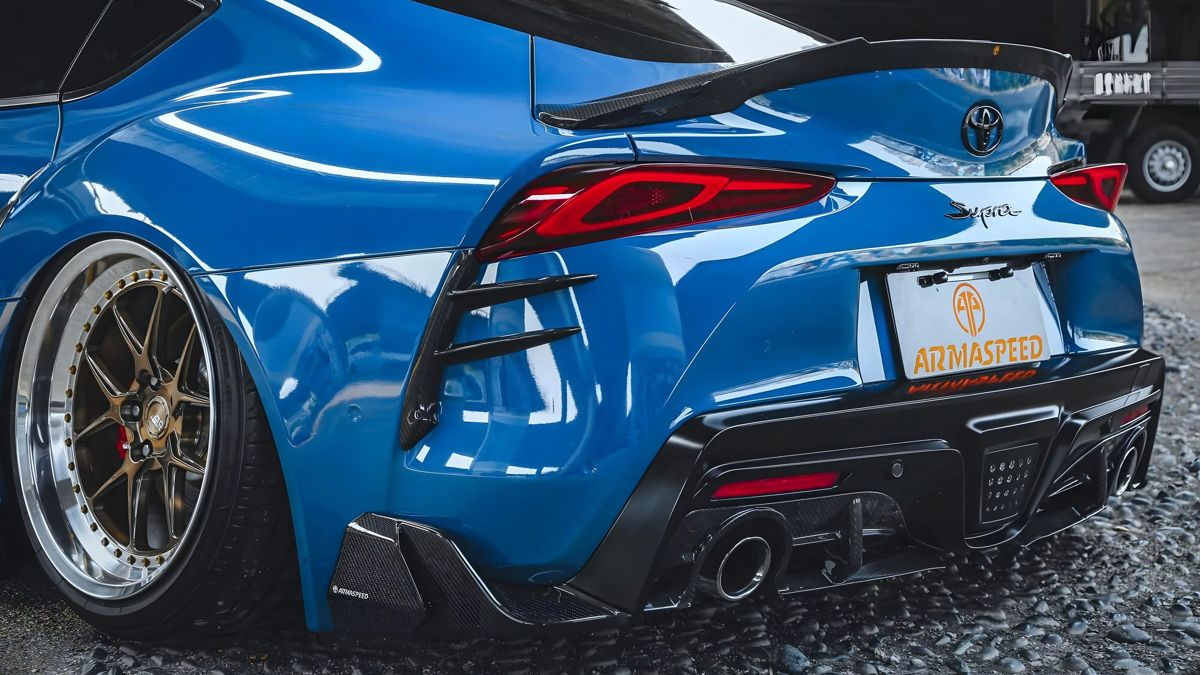Rear three-quarter view of a blue Toyota Supra A90 fitted with an ARMASPEED carbon fiber wing and diffuser.