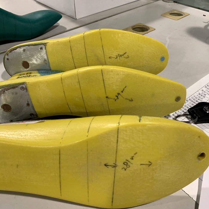 Three yellow shoe lasts hand-annotated with millimeter markings (29mm, 28mm) on a workshop shelf — the physical forms a boot is built around.