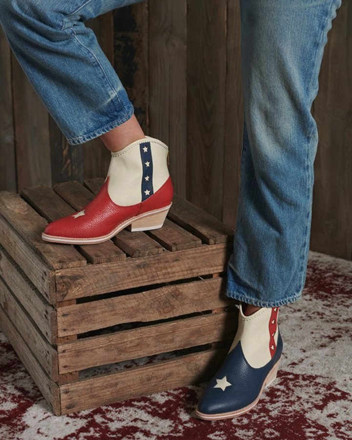 Flag Boots, red and navy star-embellished, one foot stepping on a wooden crate, paired with light-wash jeans.