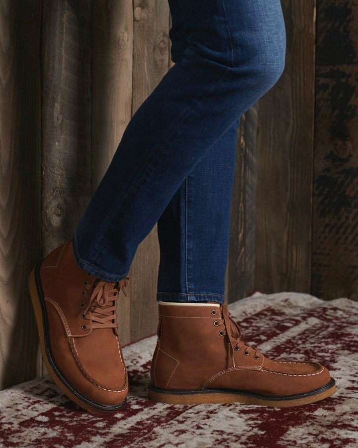 Tan smooth-leather moc-toe lace-up work boot on red-spattered concrete with blue jeans.
