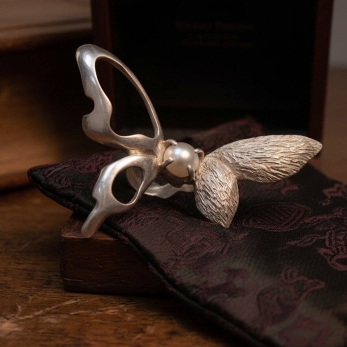 The ring piece, shown from a low rear angle, with a small pearl set in the center of a butterfly form.