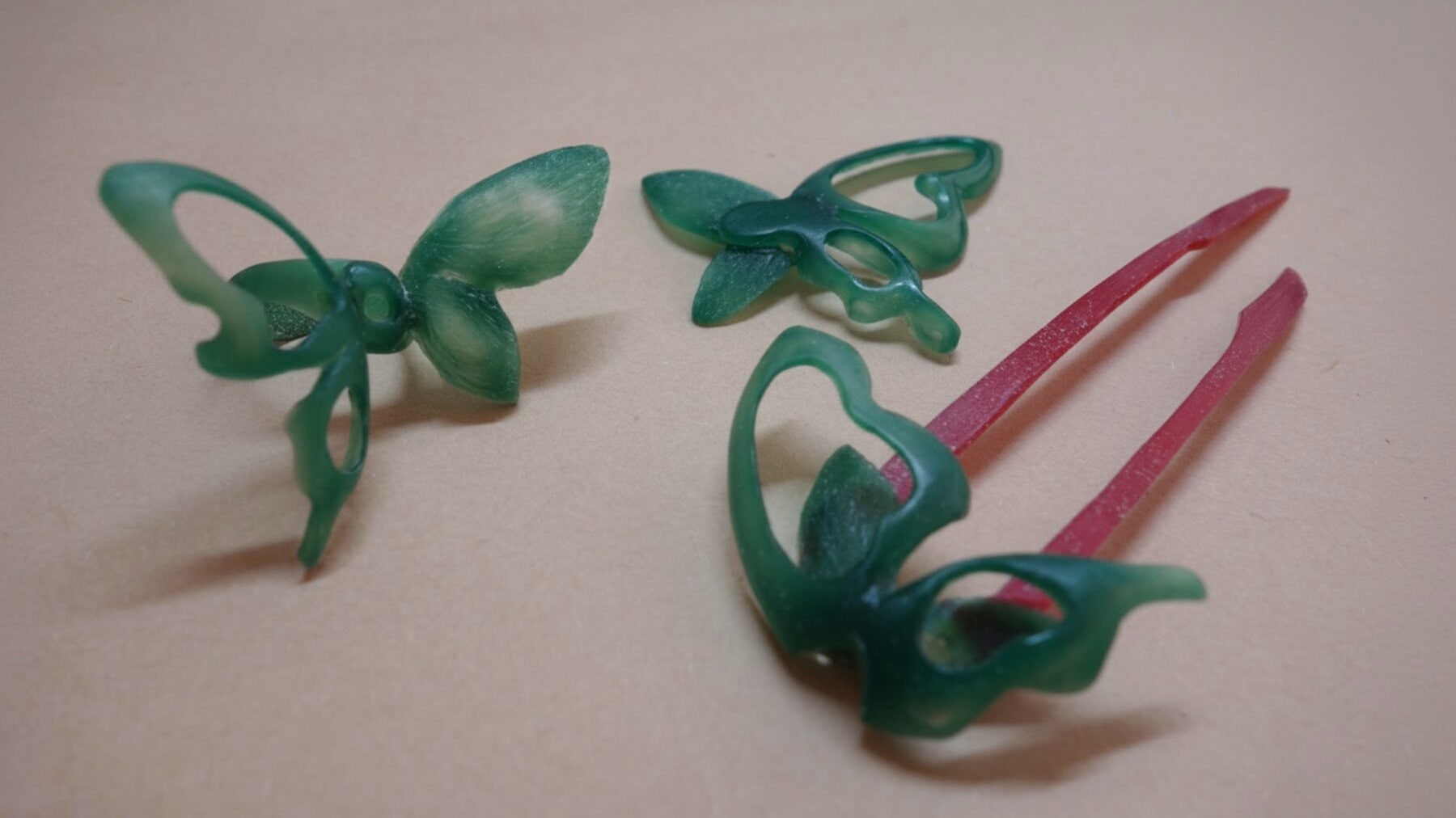 The three Liang-Zhu pieces in green carving wax, with red sprues attached, arranged on a tan work surface.