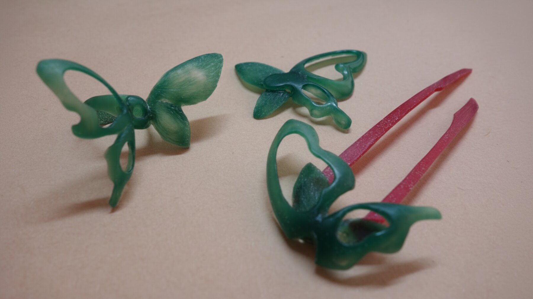 The three Liang-Zhu pieces in green carving wax, with red sprues attached, arranged on a tan work surface.