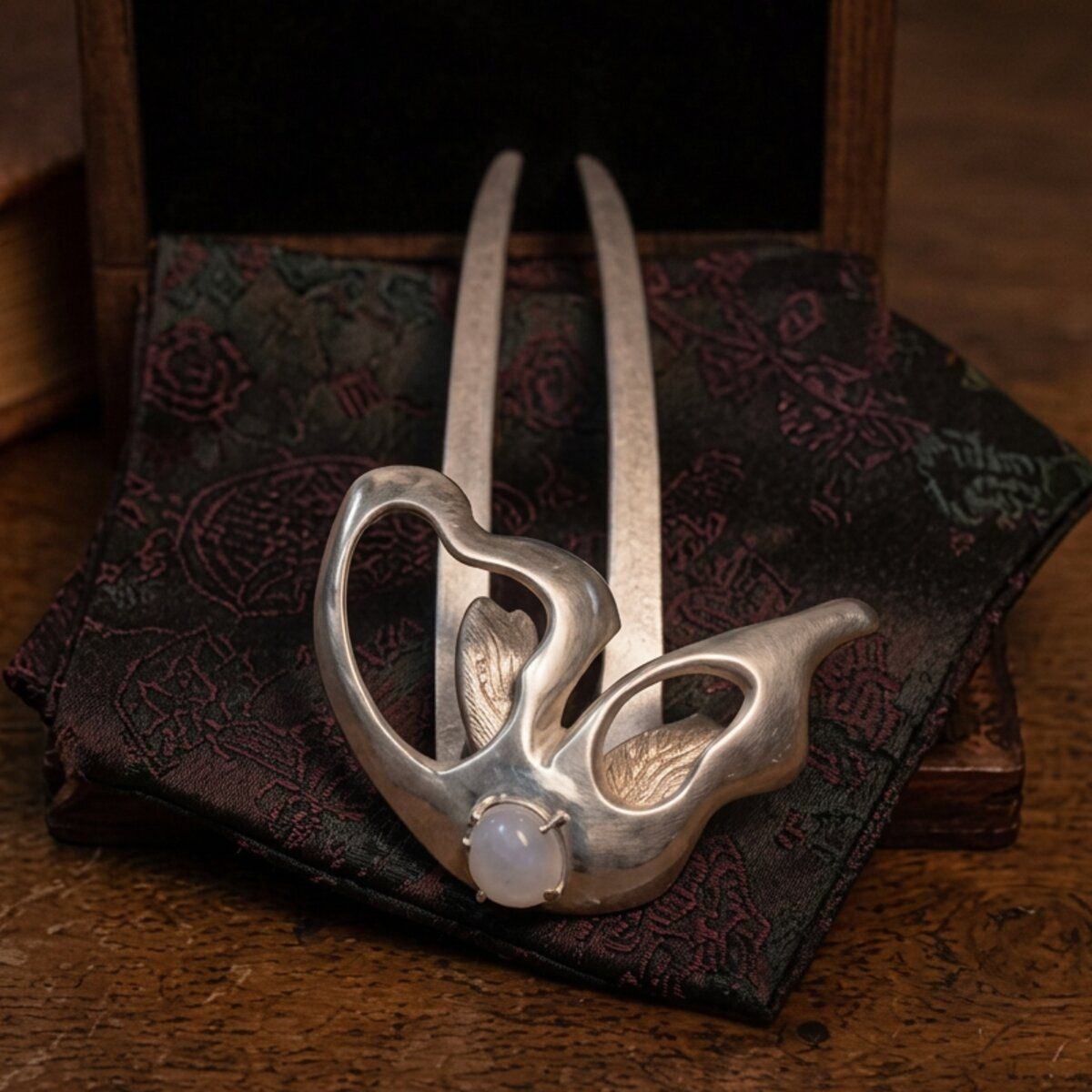 The hairpin piece, shown straight on, with a moonstone set into the head and a long curved tine.