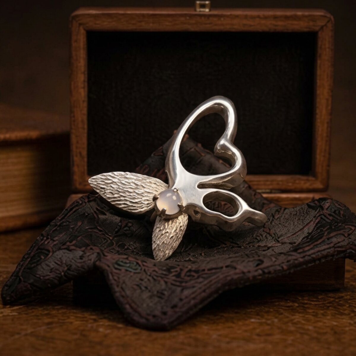 The butterfly brooch, shown from a low angle, with finely textured wings and a moonstone at the center.