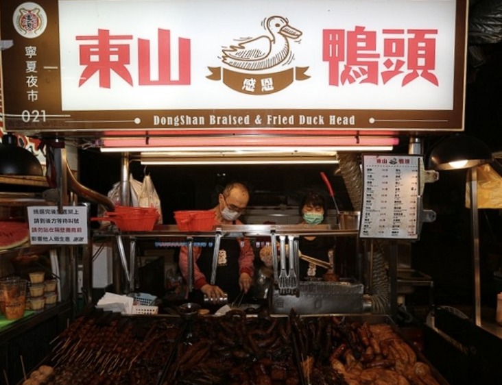 A wooden hanging banner at a Taiwan night market reading 東山鴨頭.