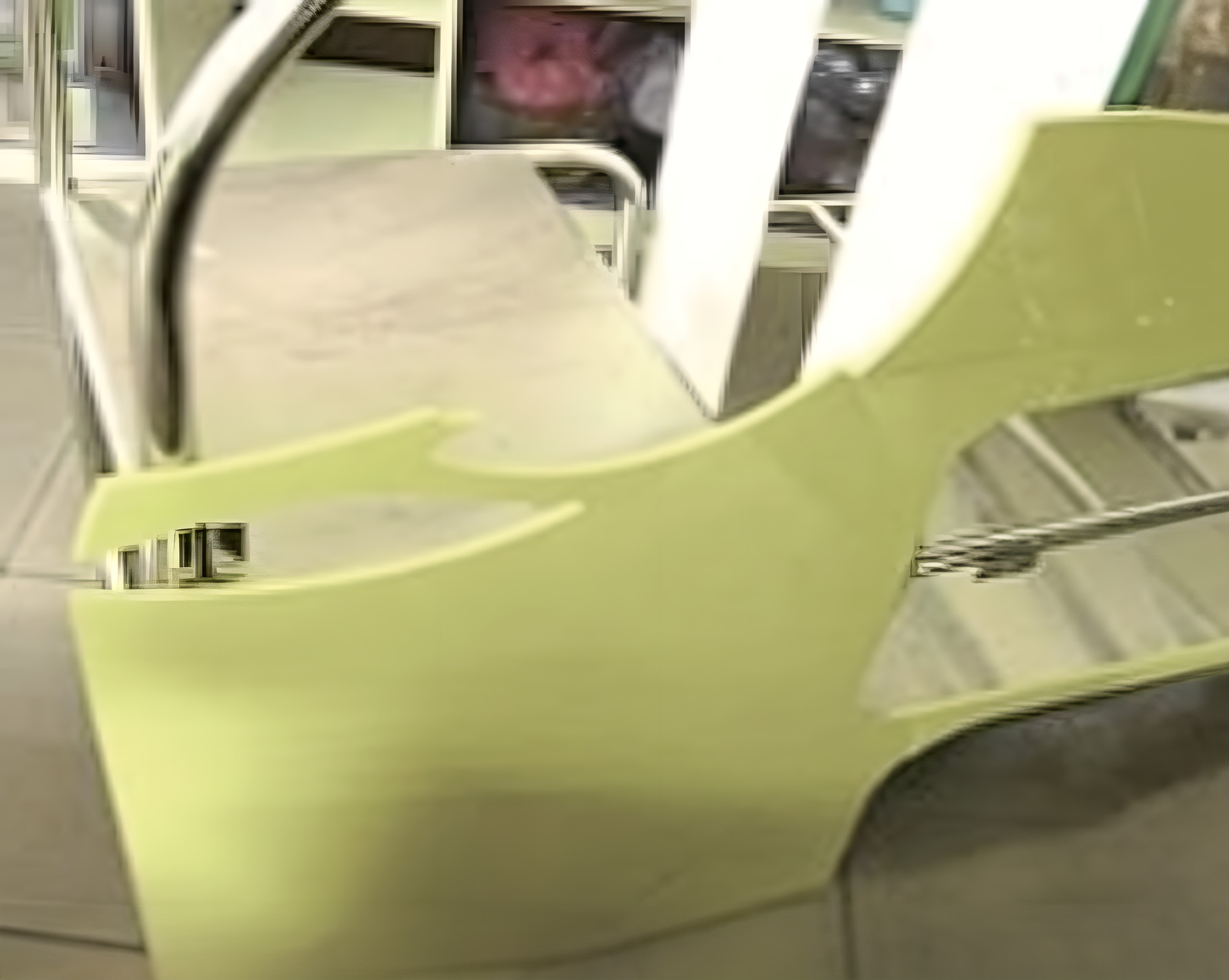 Yellow-green CNC-cut ABS body panels being fitted to the stainless tube frame, photographed close-up against the workshop background.